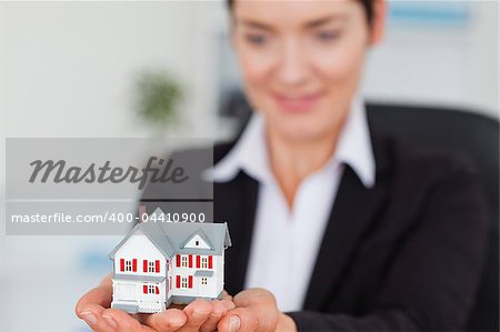 Smiling businesswoman holding a miniature house with the camera focus on the objecty