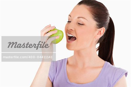 Lovely woman eating an apple while standing against a white background