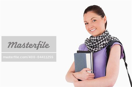 Good looking student holding books and her bag while standing against a white background