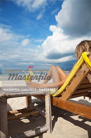 Woman sitting on deckchair and enjoying a cocktail on a tropical beach
