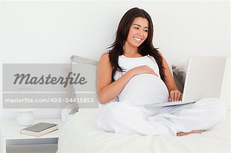 Beautiful pregnant woman relaxing with her laptop while lying on a bed at home