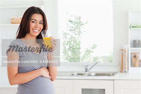 Beautiful pregnant woman drinking a glass of orange juice while standing in the kitchen
