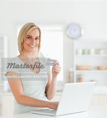 Blonde woman with credit card and notebook looks into camera in the kitchen