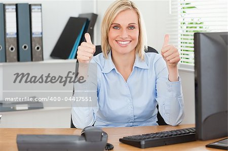 Young woman sitting behind desk with thumbs up in an office