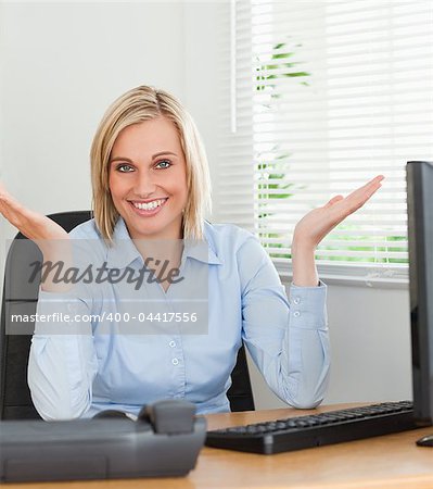 Smiling woman sitting behind desk not having a clue what to do next inan office