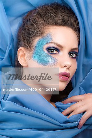face shot of a beautiful girl with glitter make up laying on purple silk