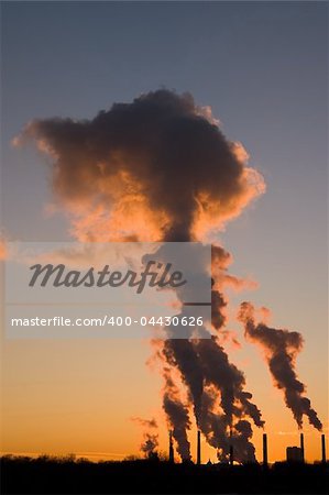 Silhouette of smoke stacks smoking into the sky at sunset