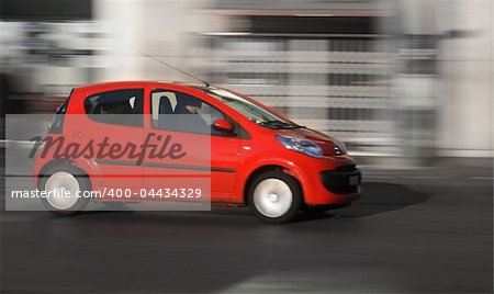 Small red generic car speeding in the city. Panning shot, not motion blur in photoshop.