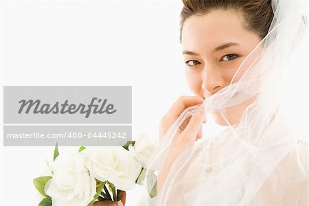 Portrait of Asian bride with bouquet and pulling veil over face.