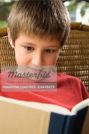 Caucasian pre-teen boy reading book.