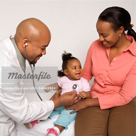 African-American male doctor examining baby girl with mother watching.