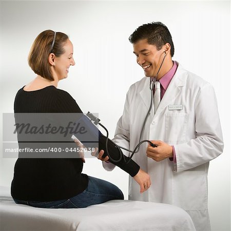 Asian American male doctor testing blood pressure of pregnant Caucasian woman.