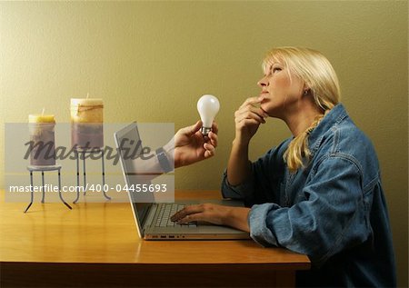 Attractive businesswoman deep in creative thought while a hand holding a light bulb comes out of her screen. Concept: Internet Inspiration, creative thinking online, ideas, etc.