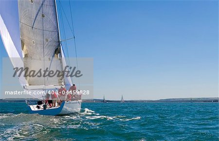 A fully crewed racing yacht sailing on a glorious summer's day