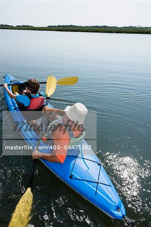 Back view of African American middle-aged couple paddling kayak.