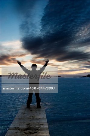 A man standing on the edge of a frozen lake at sundown