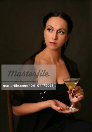 The beautiful woman with a glass of martini on a dark background