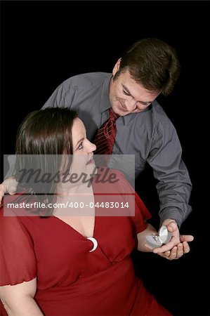 A man pops the question to his girlfriend by giving her an engagement ring.  Black background.