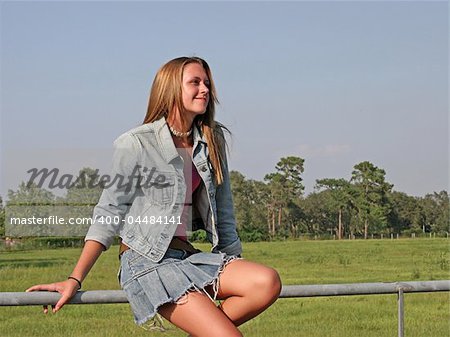 A beautiful girl sitting on a fence in the country, looking toward heaven.