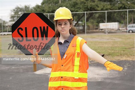 A female construction worker slowing traffic with a road sign and hand gesture.