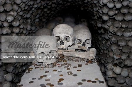 At the Sedlice All Saints bone church in Kutna Hora, a display of skulls is surrounded by donations of various coins. The walls surrounding the skulls are made of various bones from legs and arms. A scary image for Halloween.