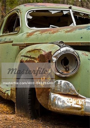 The front view of a green hardtop abandoned in the woods