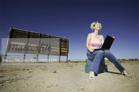 Woman with a laptop computer outside in front of an old bilboard.
