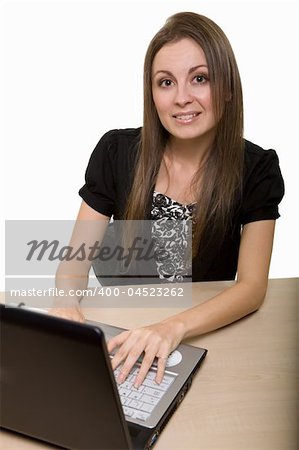 Attractive young brunette woman in business suit sitting at a desk typing on a computer keyboard and looking at camera over white