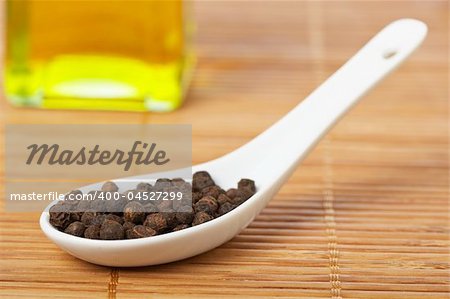 Peppercorns in the spoon and oil bottle for prepare tasty food with soft shadow in the bamboo mat background. Shallow depth of field