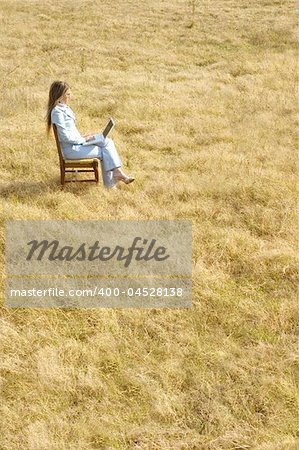 A young business woman working on a laptop in the middle of a dry field.