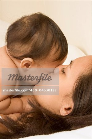 Mom and son lying down on bed and mother kissing the infant baby