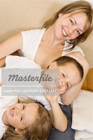 Woman and kids in white shirts laying on the sofa laughing