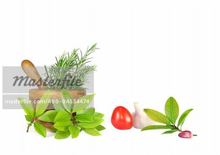 Fresh herb selection of rosemary and bay leaves with an olive wood pestle and mortar and ripe tomato with a garlic bulb and clove. Over white background.
