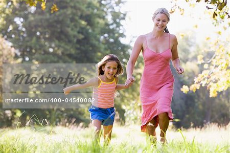 Woman and young girl running outdoors holding hands and smiling