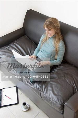 A young professional woman working from home with her laptop and coffee on the sofa