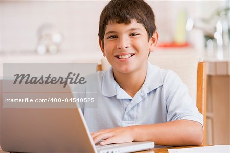 Young boy in kitchen with laptop and paperwork smiling