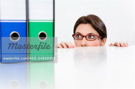 Young businesswoman peering in curiosity from behind desk with folders