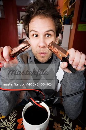 Young man holding jumper cables coming out of coffee mug