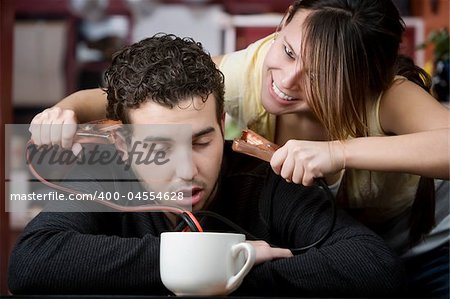 Young woman holding jumper cables coming out of coffee mug to man's head