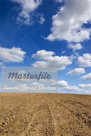 Blue sky with clouds over ploughed field.