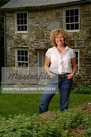 an attractive woman stands before a stone house