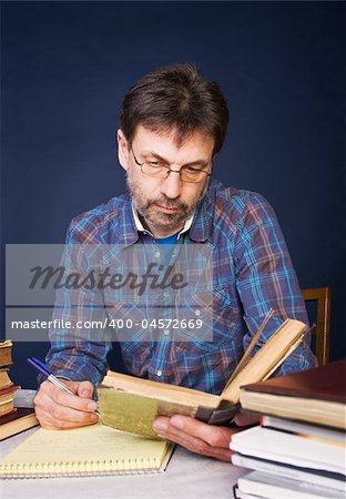 Researcher taking notes; he is surrounded by heaps of books.