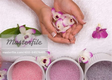 Pedicured hands, different kinds of cyrstal bath salts, lotions, massage oils, towel, mint and exotic orchids