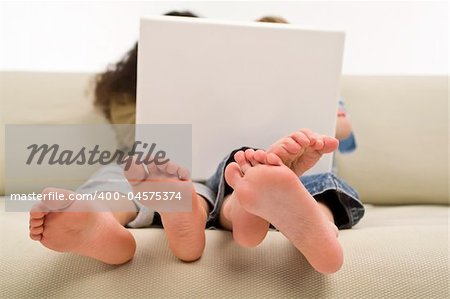 Two young children surfing the wold wide web on a laptop while sitting on a settee