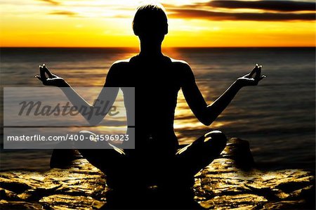 silhouette of woman on rock in the sunset sea in a classic yoga pose