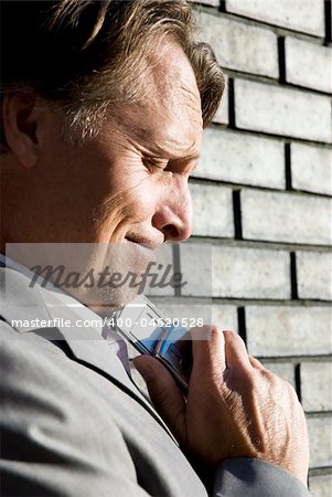 a stressed and upset forties businessman stands in front of a brick wall with his cellphone pressed against his chin after hearing bad news.