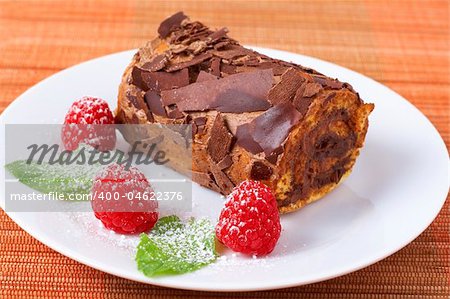 Miniature chocolate swiss roll cake served on a plate with mint leaves and raspberries on orange background