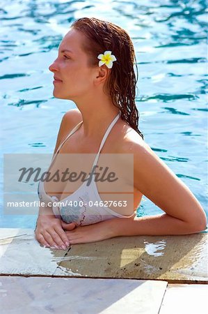 Beautiful brunette girl with tropical flower in her hair in the hotel pool