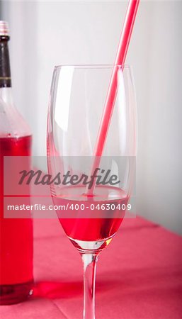 Red cocktail in a glass with a straw and a bottle
