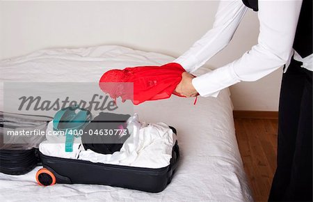 Full suitcase on a bed and a woman adding a red dress